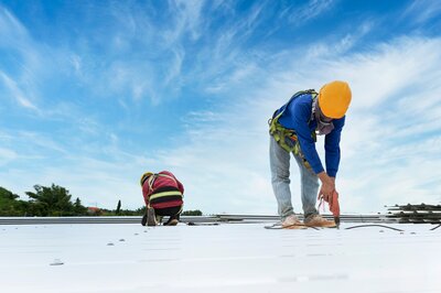 Two contractors installing a metal roof on a commercial building