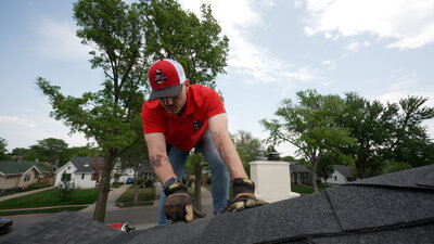 A Mighty Dog Roofing inspector on a roof, pointing at a potential issue during a roof inspection