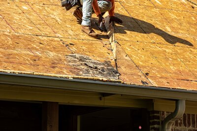 A roofer inspecting rotted roof decking near a gutter