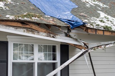 Damaged roof with a hole partially covered by an emergency tarp, illustrating the need for urgent roof repairs